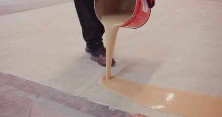 Worker coating floor with epoxy resin in an industrial hall.