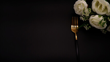 Golden fork placed on black background. Table setting idea of a fork and white flower with a black...