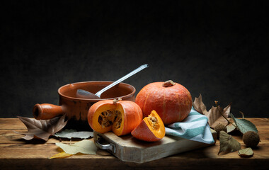 Pumpkins on rustic wooden table with old terracotta pan, dry leaves and dark gray background, space for text.
