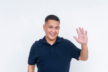 A neighborly middle-aged Asian man in a casual polo shirt waving hi with a warm smile, isolated on...