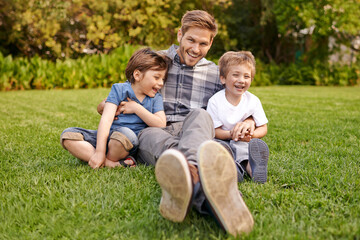 Naklejka na ściany i meble Smile, nature and portrait of kids with father relaxing on grass in outdoor park or garden. Happy, family and excited boy children sitting on lawn with young dad for bonding in field together.