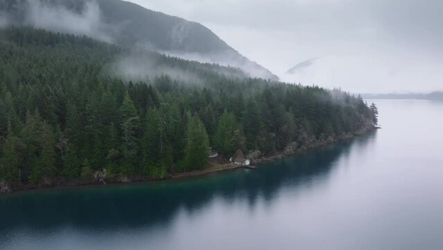 Lake Crescent in Olympic National park. Scenic Washington nature 4K USA. Aerial view of mountain forest cabin at scenic lake. Cinematic rustic house hidden in evergreen rainforest covered by dense fog