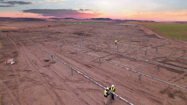 Aerial view of electrical power plant under construction with workers assembling metal frame parts for solar panels for producing solar electric energy. Development of renewable electricity in Spain