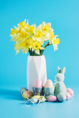 Happy Easter greeting card. soft pastel green Easter bunny figurine and collection of colorful, decorated Easter eggs against a vibrant blue background. - 746324469