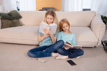 Two sisters reading book in home. digital detox. children having fun together. Happiness is in small things, slow living, education in home concept.