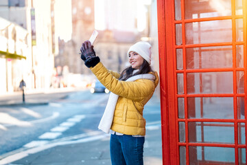 Outdoor portrait of woman using camera against red phonebox in English city