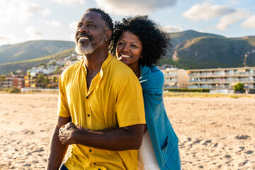 Beautiful mature black couple of lovers dating at the seaside - Married african middle-aged couple bonding and having fun outdoors, concepts about relationship, lifestyle and quality of life - obrazy, fototapety, plakaty