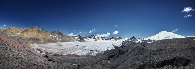 Expansive glacier sweeps across a mountainous landscape under a clear blue sky, panoramic view. Mountain valley landscape
