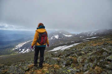 Alone hiker gazes across a vast mountainous terrain, enveloped in the soft light of an overcast sky