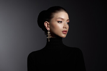 Woman with elegant makeup and a cross earring poses in a black turtleneck, exuding sophistication