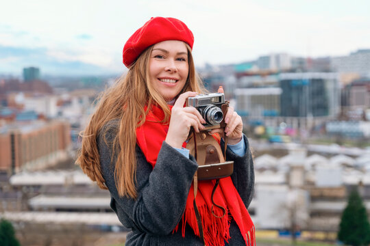 happy  woman in a grey coat, red scarf and beret  sitting in front of the city Sheffield  and taking photos on great spring day. Travel lifestyle concept