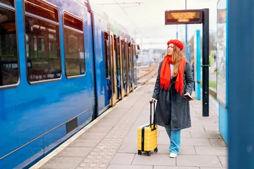 Foto op Canvas Happy tourist woman with small yellow luggage at the train station exited about oncoming journey. Enjoying travel by train concept © Iryna