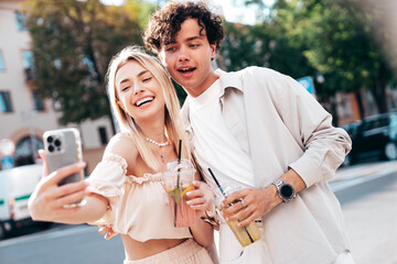 Young smiling beautiful woman and her handsome boyfriend in casual summer clothes. Happy cheerful family. Female having fun. Couple posing in street. Holding and drinking cocktail drink in plastic cup