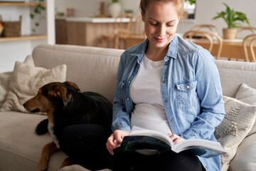 Caucasian pregnant woman sitting on sofa and reading a book