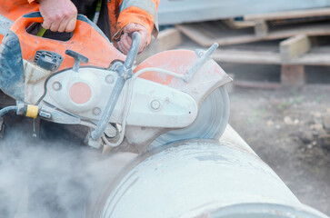 Construction worker cutting concrete pipe for drainage using a cut-off saw. Cutting concrete with a...