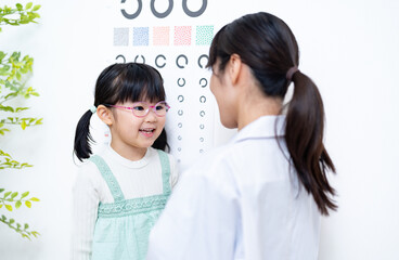 視力検査表の前で話す女性医師と女の子