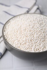 Tapioca pearls in bowl and towel on white tiled table, closeup