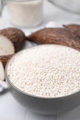 Tapioca pearls in bowl and cassava roots on white tiled table, closeup