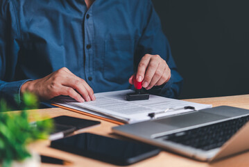 A person's hands are seen stamping a document, symbolizing the approval process in a professional...