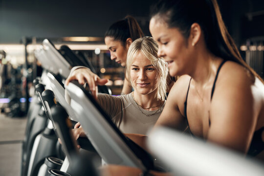 Smiling female instructor helping a fit young woman with her stationary bike settings during a cardio exercice class at a health club