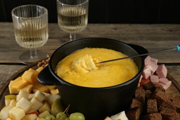 Fondue pot with melted cheese, glasses of wine and different products on wooden table, closeup