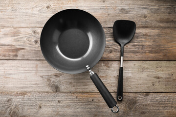 Black metal wok and spatula on wooden table, top view