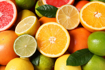 Different fresh citrus fruits and leaves as background, above view