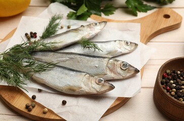 Fresh raw sprats, peppercorns and dill on light wooden table, closeup