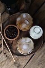 Refreshing iced coffee with milk in glasses, ingredients and straws on wooden table, flat lay