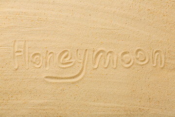 Word Honeymoon written on sand, top view