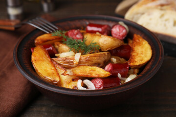 Delicious baked potato with thin dry smoked sausages, onion and dill in bowl on wooden table, closeup