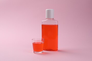 Fresh mouthwash in bottle and glass on pink background