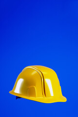 Fototapeta premium Hard hat for Labour Day concept, 3d render. Yellow helmet isolated on blue vertical background with copy space. 