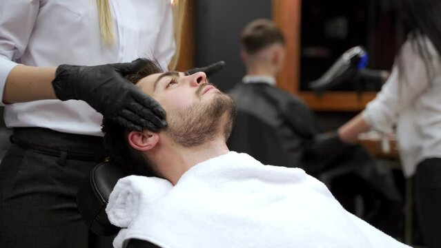 Barber gives client relaxing neck, face massage. Male enjoys expert hands at grooming session. Wellness in mens salon. Professional stylist provides luxury service, facial care for customer comfort.