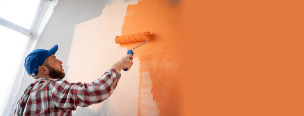 Repair, building and home concept. male in workwear painting wall with roller brush