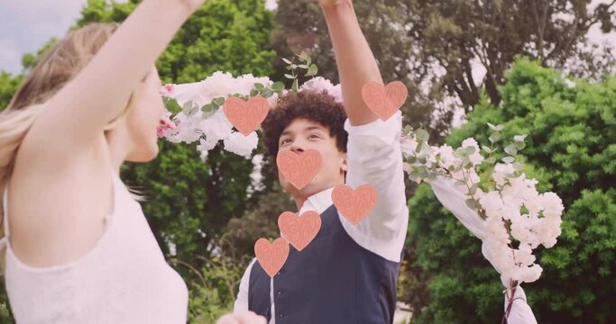Animation of pink hearts over happy diverse couple dancing in garden on wedding day