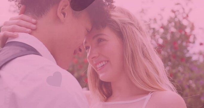Animation of hearts and pink tint over happy diverse couple embracing at outdoor wedding