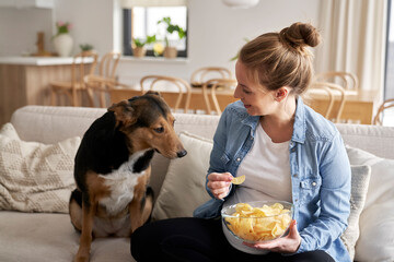 Pregnant woman eating crisps and playing with a dog
