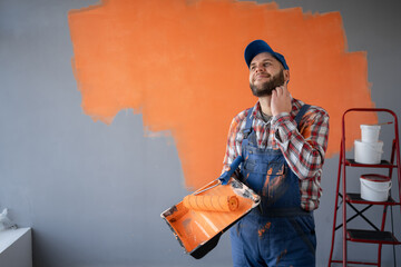 Painter man holding a paint roller and tray having doubts and with confuse face expression standing...