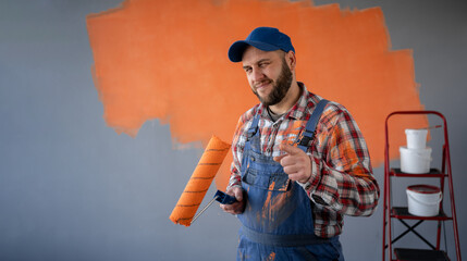 Painter man holding a paint roller pointing front with happy expression standing in new flat