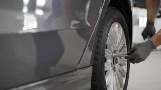 Auto mechanic attaches alloy wheel to luxury sedan using torque wrench in high-end garage. Professional, precise tire installation ensures safe, optimal vehicle performance. Expert secures rim.
