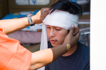 An accident victim man receiving medical attention, a bandage wrapped around his head from a...