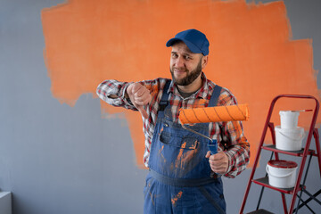 Painter man holding a paint roller showing thumb down with negative expression