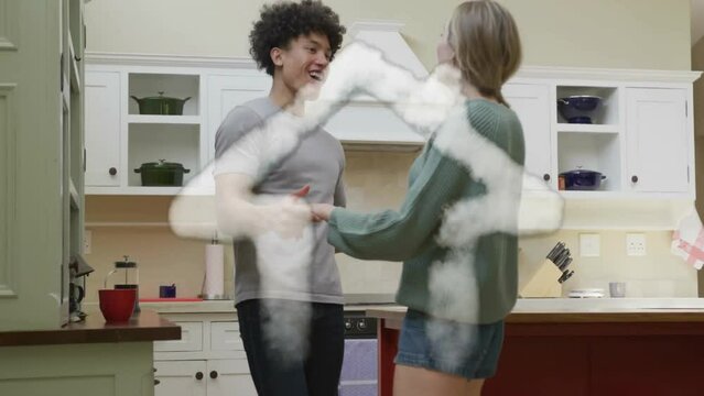 Animation of cloud house over happy diverse couple dancing together in kitchen