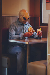 One man with alien mask eating alone inside a fast food store bad food hamburger and french fries....