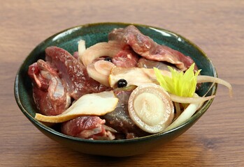 Deer meat  marinated in red wine with bakon, onion, garlic and juniper berries.  Bowl with pieces of deer meat on  wooden table.