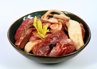 Deer meat  marinated in red wine with bakon, onion, garlic and juniper berries.  Bowl with pieces of deer meat on white background.