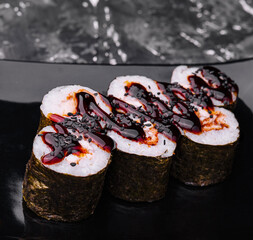 sushi roll maki with eel and unagi sauce on a black plate