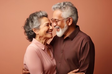 
Senior couple, both in their late 65s, Hispanic, sharing a warm embrace against a gentle peach pastel background with copy space