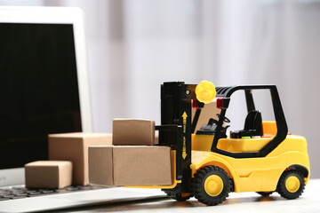 Toy forklift with boxes near laptop on table. Logistics and wholesale concept